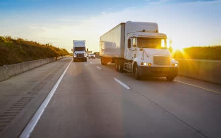 two semi trucks on an open road as the sun sets in the background