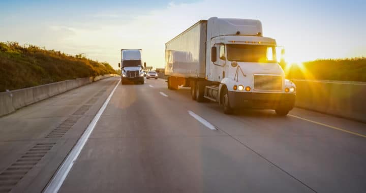 two semi trucks on an open road as the sun sets in the background