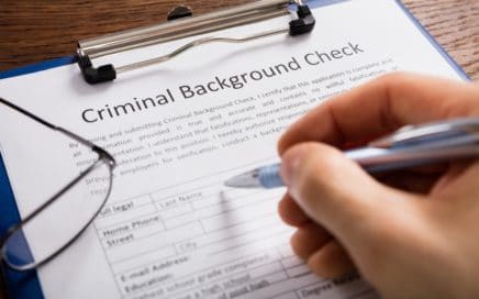 Close-up Of Person Hand Filling Criminal Background Check Application Form