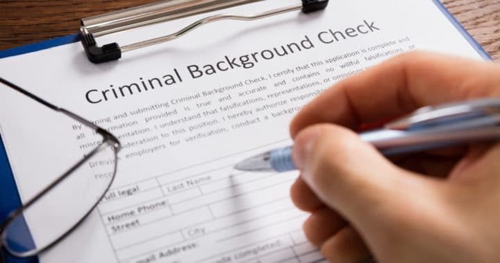 Close-up Of Person Hand Filling Criminal Background Check Application Form
