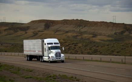 Truck is driving down an empty highway past a mountainous landscape.