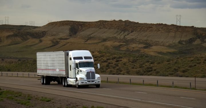 Truck is driving down an empty highway past a mountainous landscape.