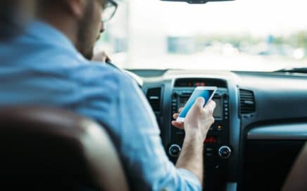 a young man driving while checking his phone and looking away from the road ahead