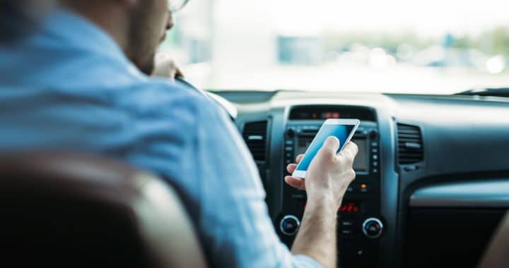 a young man driving while checking his phone and looking away from the road ahead