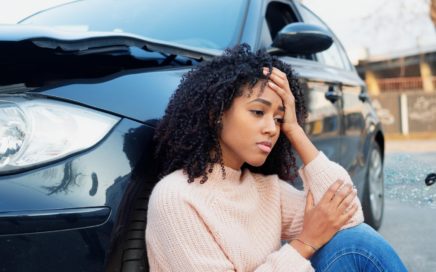 A young woman sitting next to her car after a car accident