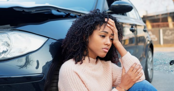 A young woman sitting next to her car after a car accident