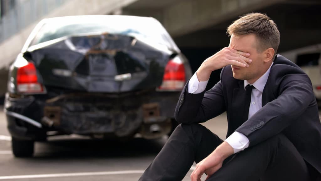 Desperate man sitting asphalt on crashed car background, automobile accident