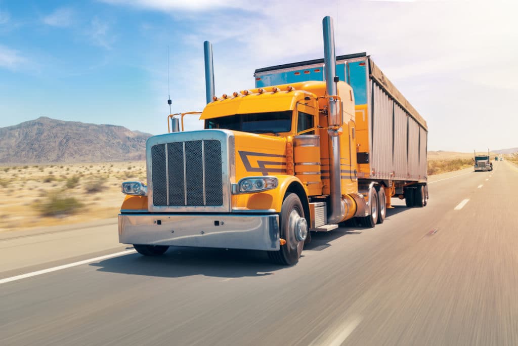 An orange Semi Truck driving down a road in New Mexico